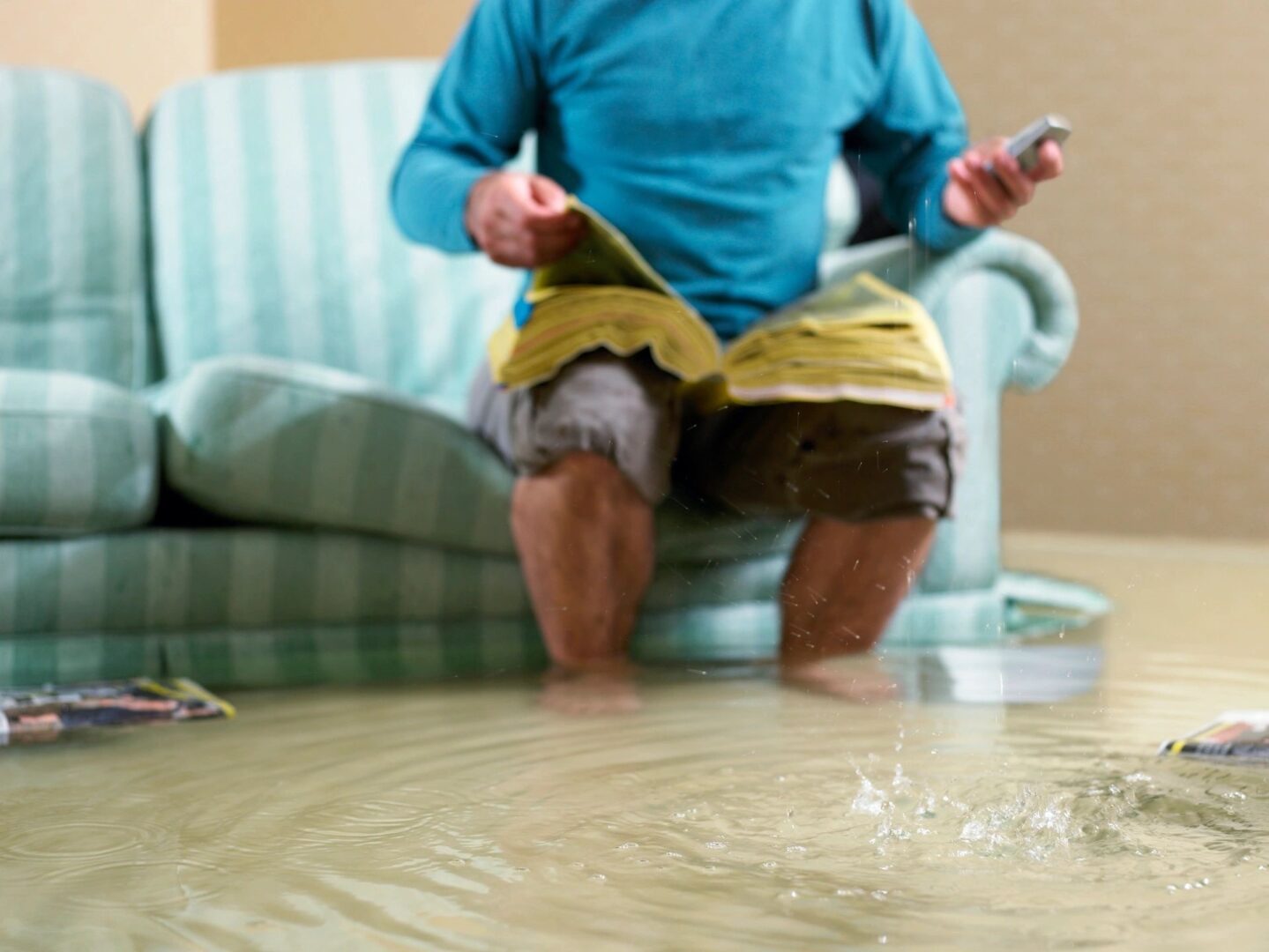 Man sitting on a striped couch while holding a wet book in a flooded room